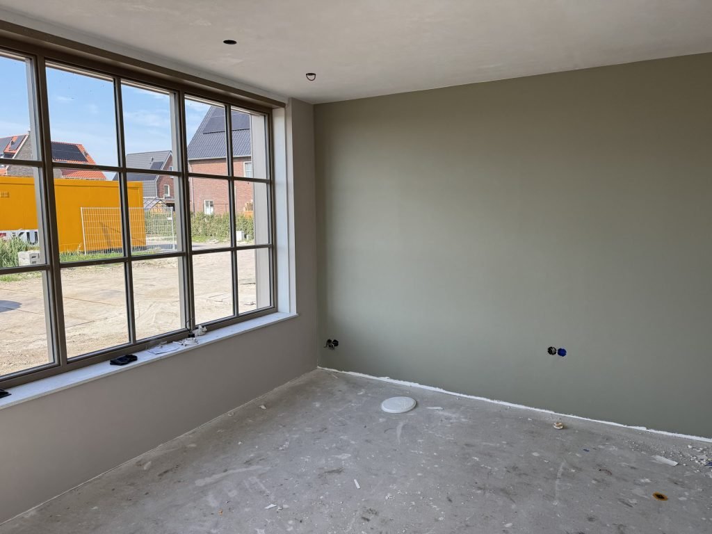 Kamer in een nieuwbouwwoning met een grijsgroen gesausde wand en een groot raam met roeden